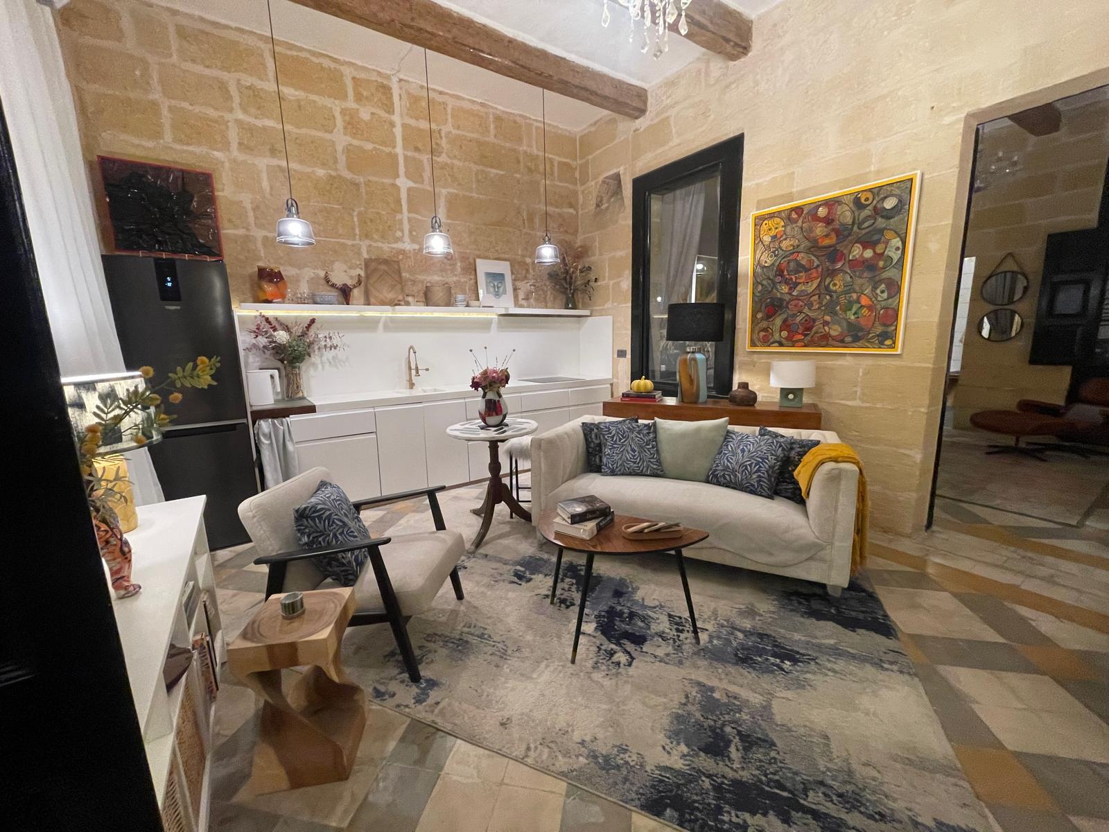 The lounge and kitchen at No. 50: limestone walls, pendant lamps, a long cream sofa, kitchen counter, and a large painting.