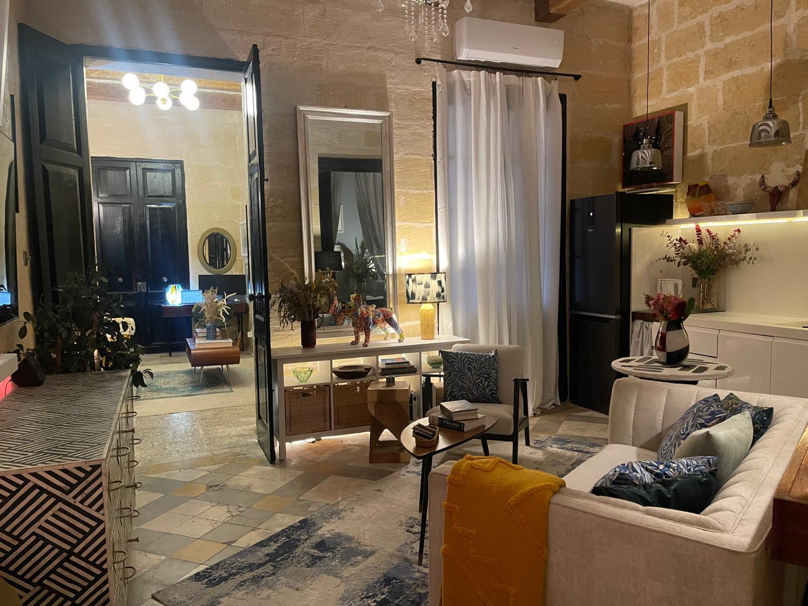 The main lounge in wide view: tall mirror, cream sofa with mustard throw, dining table and pendant lamps, terrazzo floor.