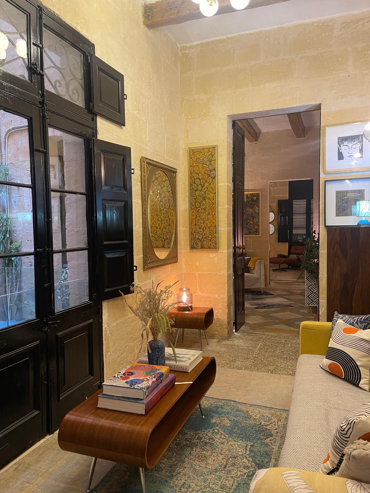 Looking through tall black doors into the yellow sitting room beyond, leather ottoman and stacked books in the foreground.